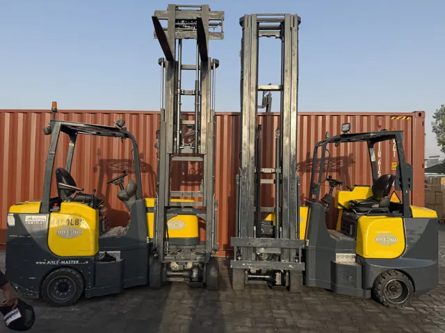 Two Aisle-Master articulated forklifts with raised masts outdoors beside shipping containers