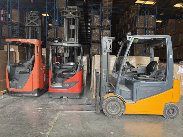 Electric forklift parked next to two reach trucks in a warehouse
