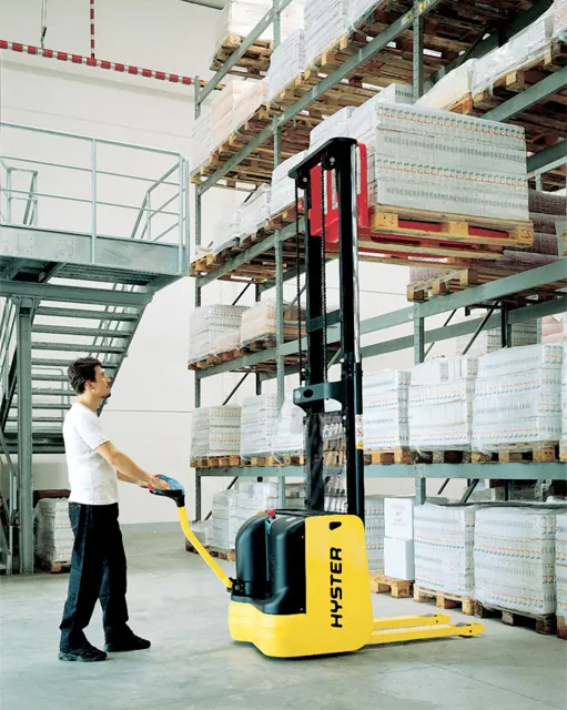 Operator using a Hyster walk-behind electric stacker beside racking