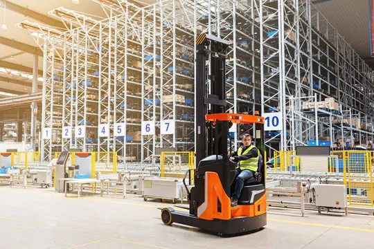 Operator driving an orange reach truck in a high-bay warehouse