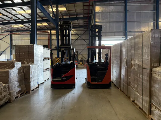 Two red reach trucks between rows of shrink-wrapped pallets