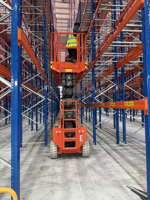 Scissor lift raised with a worker in a pallet racking aisle