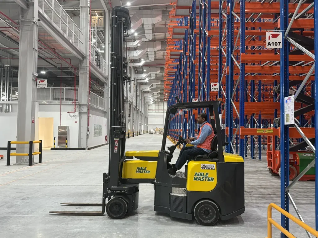 Aisle-Master articulated forklift with an operator beside high-bay pallet racking