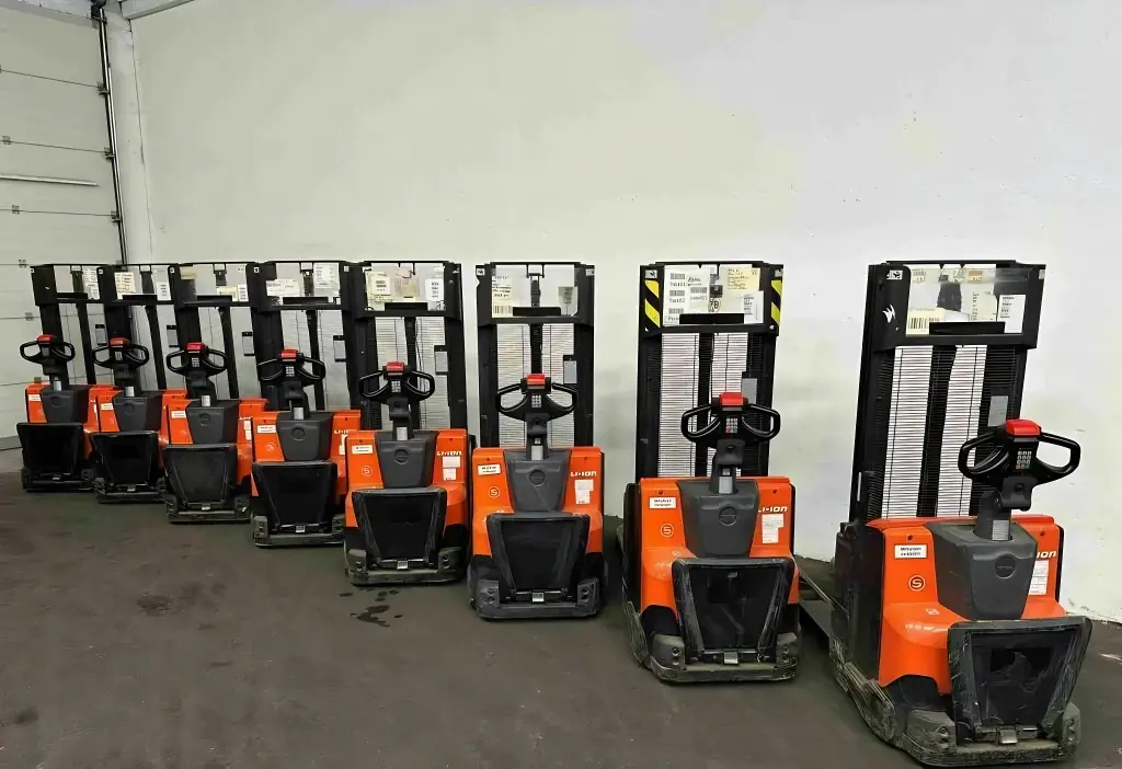 Row of electric pallet stackers parked against a wall